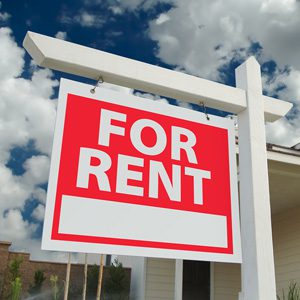 For Rent red signage in focus and a house behind