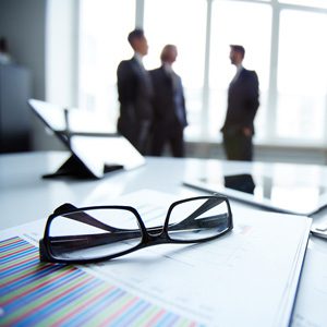 Three businessmen in a blur, eyeglasses on top of files, some ipad tablet