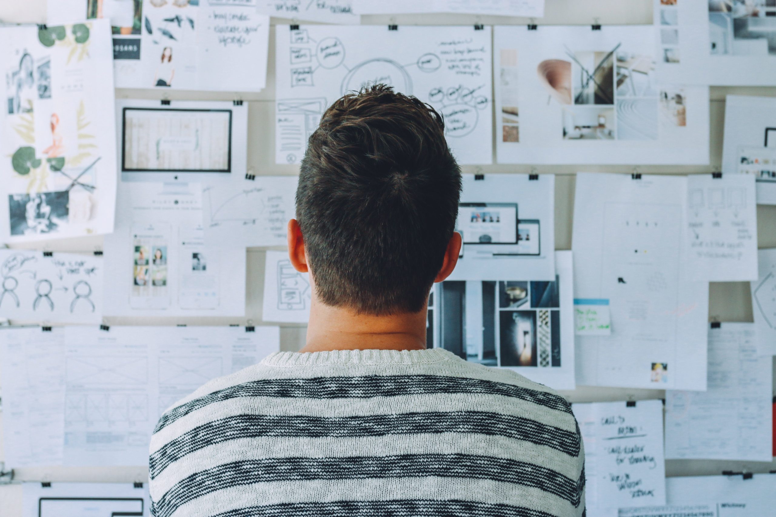 A young man stares at a bulletin board pinned with many papers and reports, much like Hoffman Realty clients seeking storm advice.