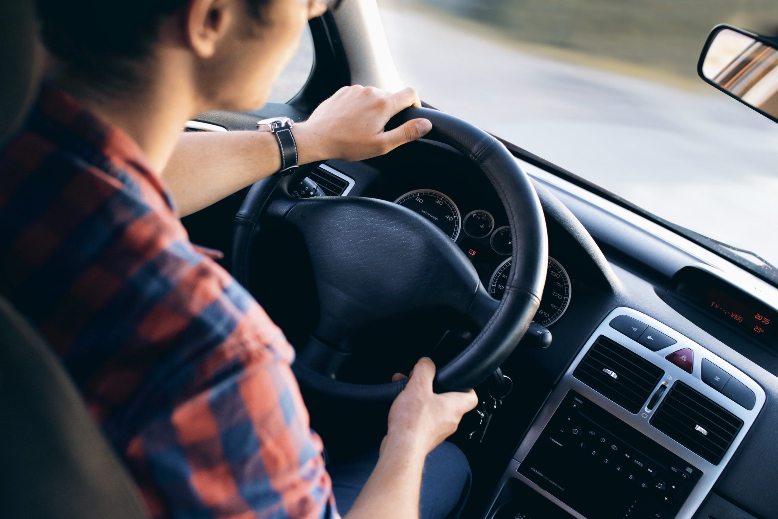 a man in checkered sleeves, holding the car steering wheel, driving