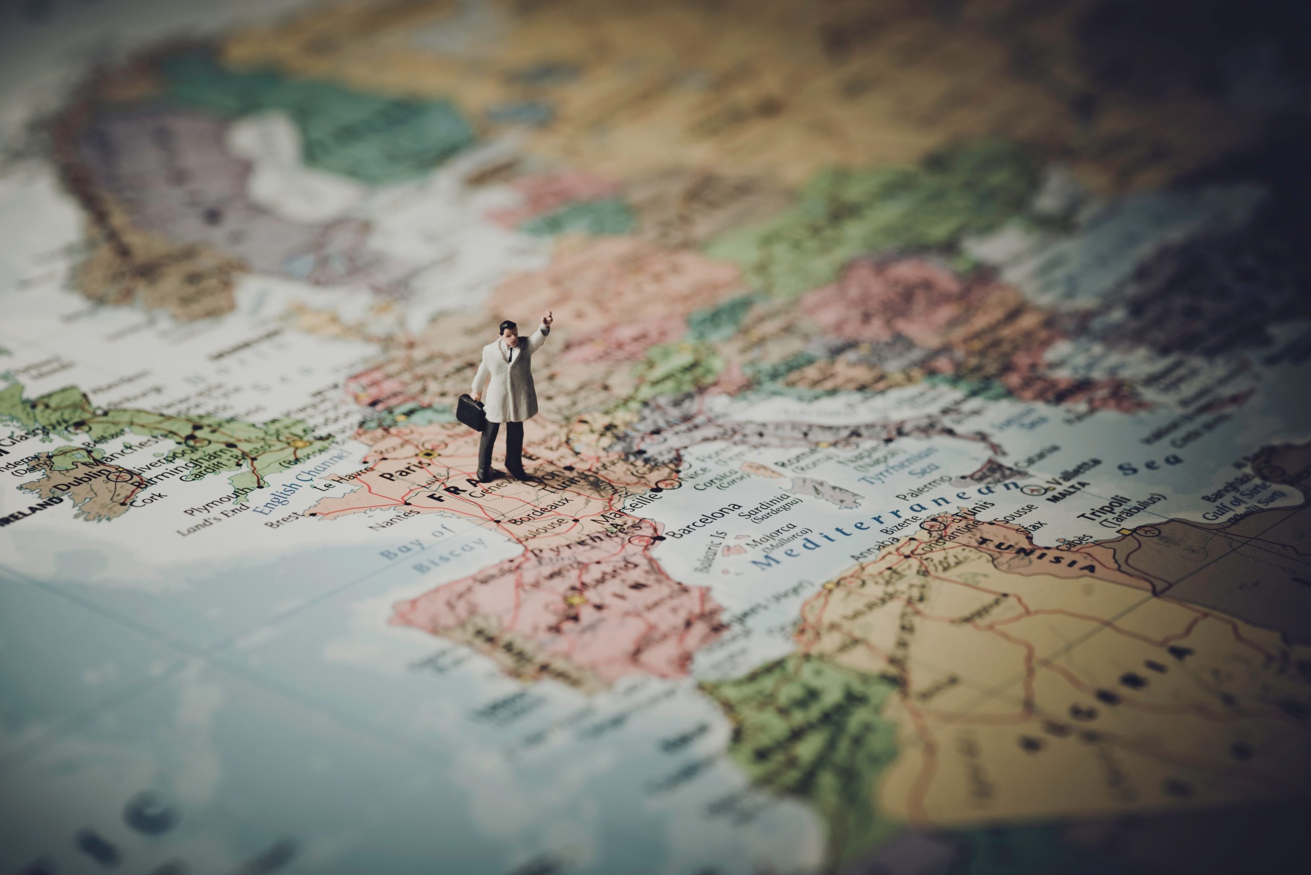  a very small miniature of a man holding his suitcase while his one hand upward, on top of a world map