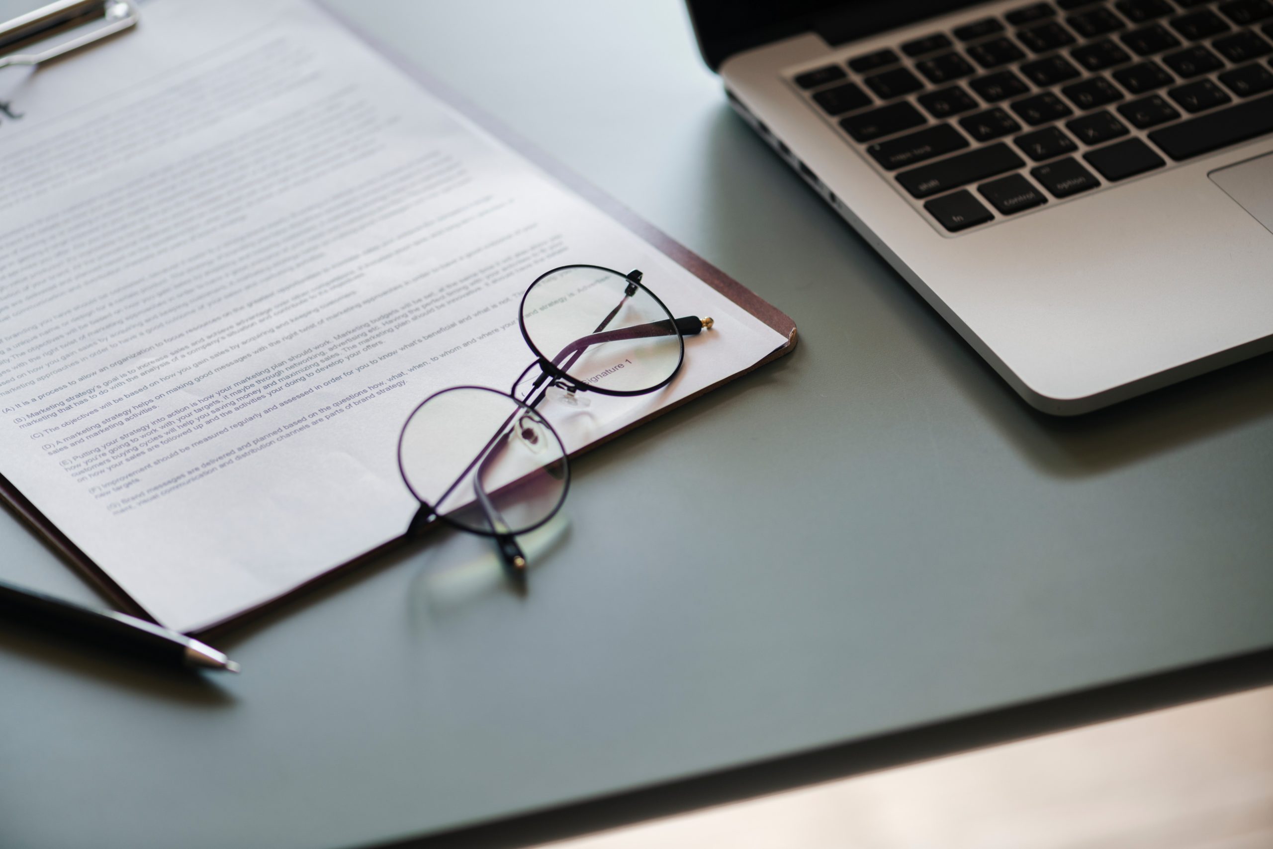 A pair of glasses sits on a contract clipped to a clipboard, next to a laptop, which tenants can use to make a maintenance request to Hoffman Realty