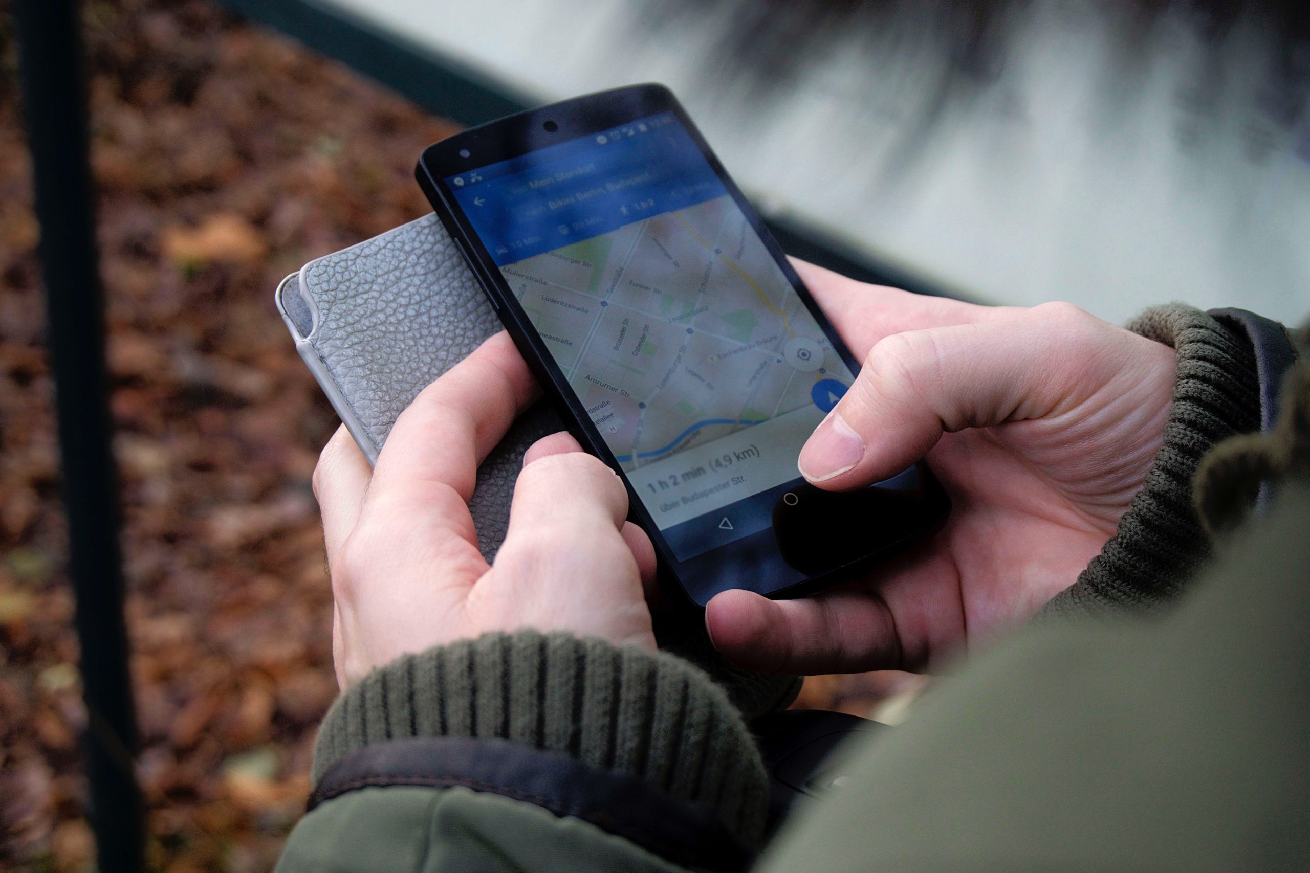 a man's hand in a green jacket, holding his phone with a map on the screen