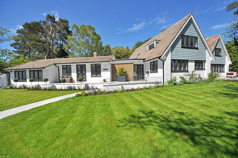 A white house with a brown roof on a large, green lawn, representative of a rental property that Hoffman Realty might offer lease terms for.