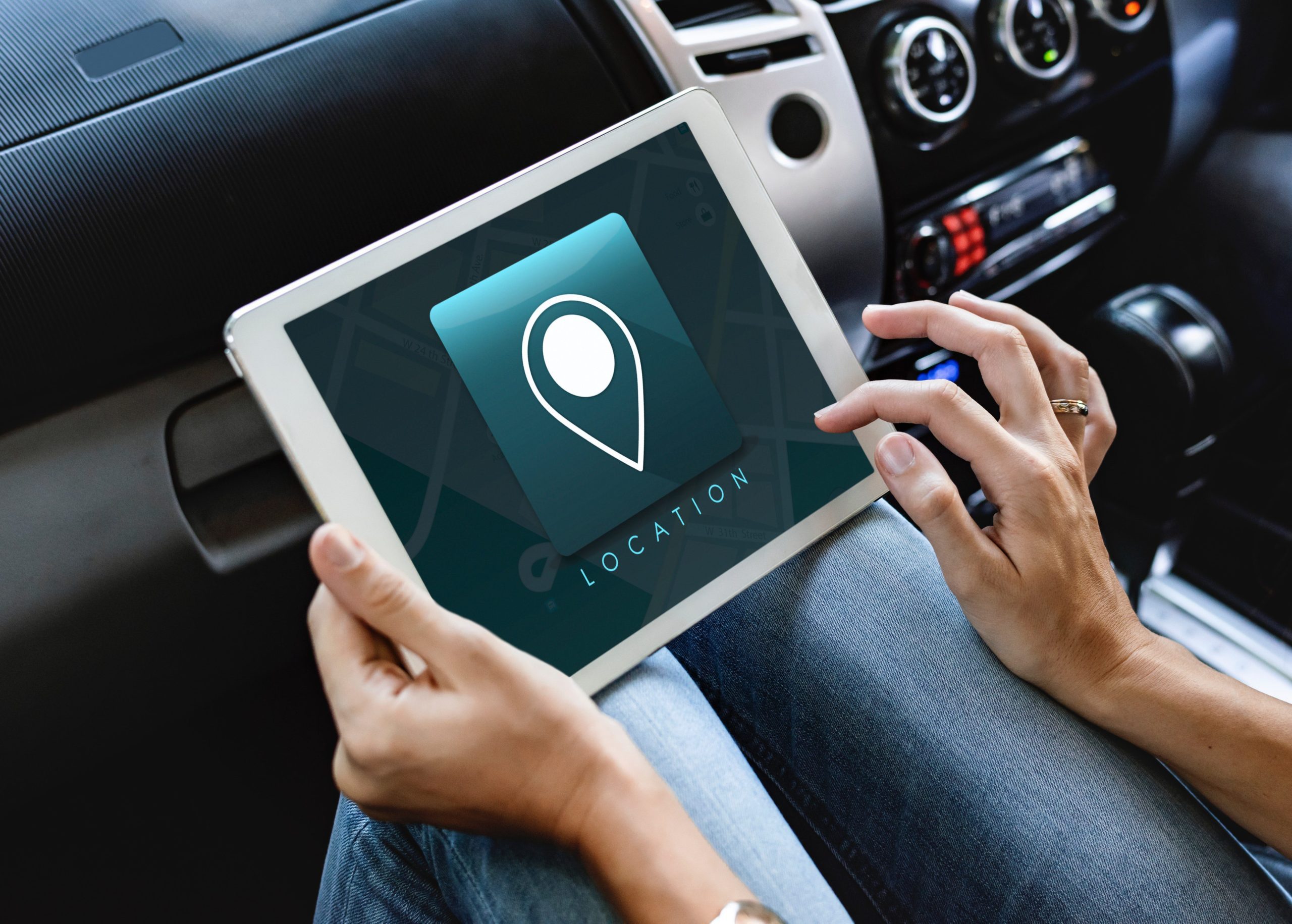 a woman's hand, inside a car, holding an iPad, with a location word and icon on the iPad screen a woman's hand, inside a car, holding an iPad, with a location word and icon on the iPad screen