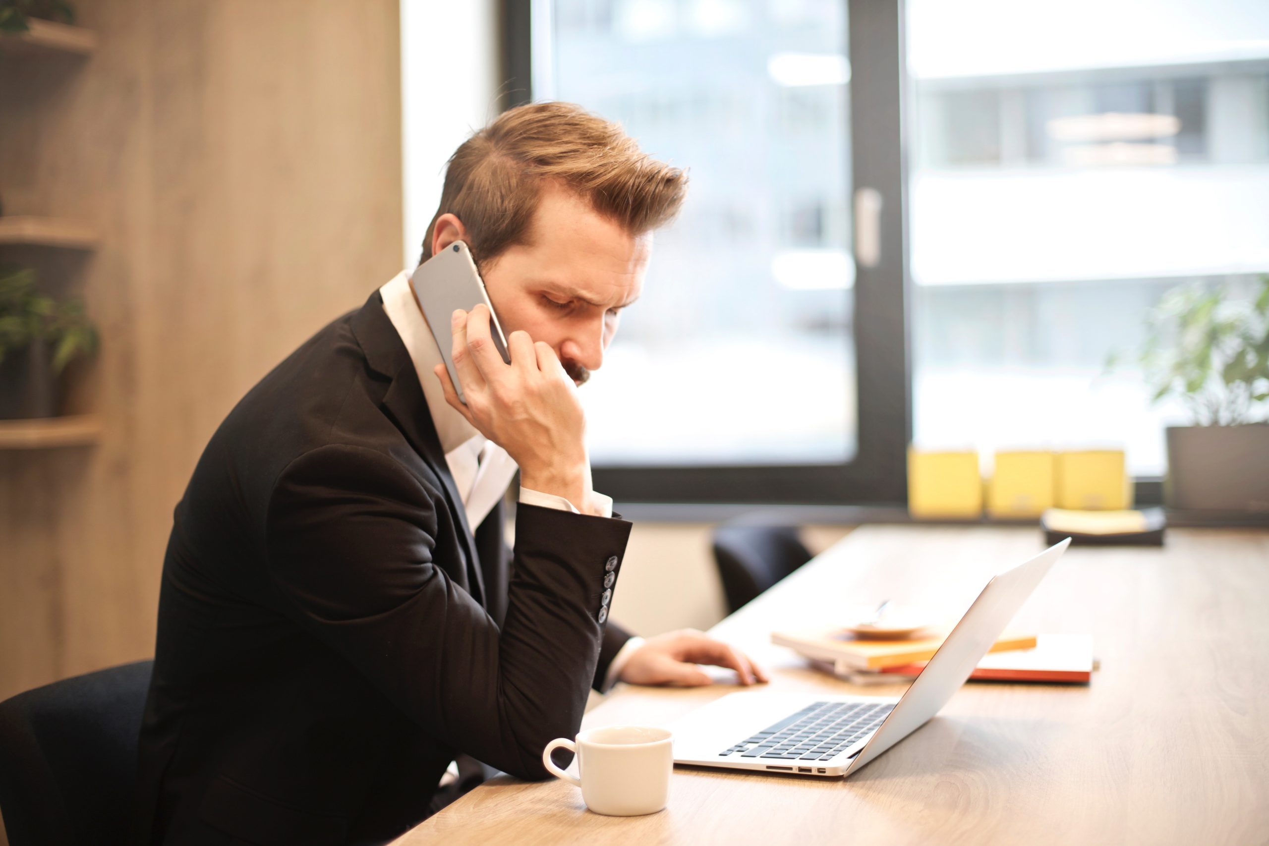 A man speaks into his cell phone at an office desk, representative of a tenant making a maintenance request to Hoffman Realty