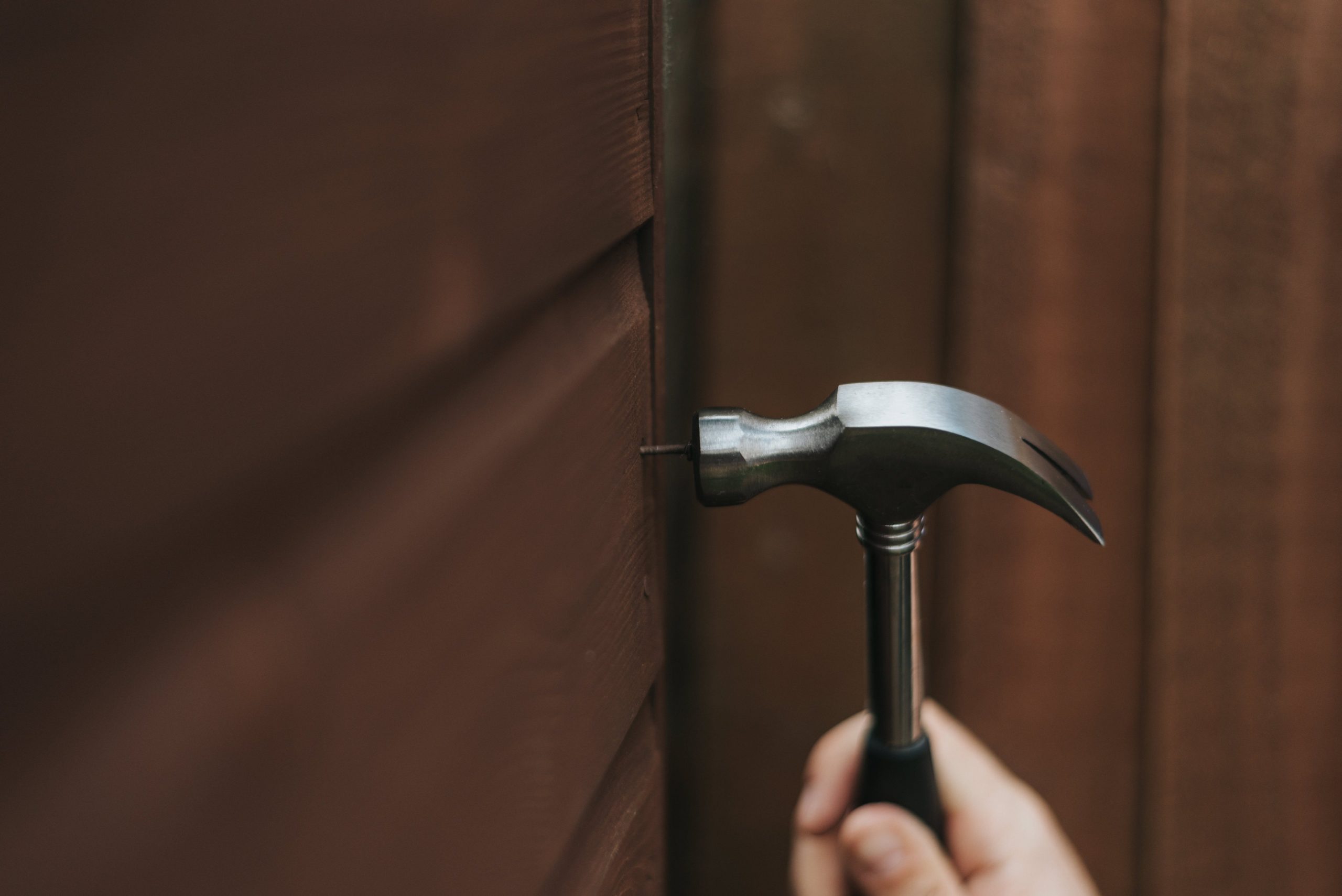 A hammer puts a nail into a piece of wood, an example of a maintenance request being filled by Hoffman Realty
